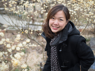 Asian women portrait - Asian female in black jacket looking and smiling to the camera. Background is yellow flower.