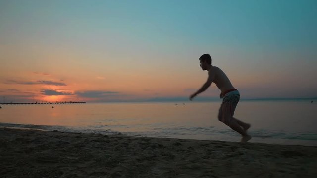 Steadicam slow motion shot of young man making cartwheel on the beach at sunset.