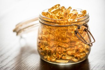 Omega 3-6-9 fish oil yellow softgels on wooden black board into airtight glass jar