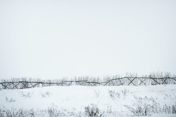foggy landscape with fence snowy field in a countryside