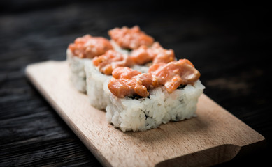 closeup of a set of sushi rolls with salmon topping on wooden board