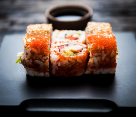 close up of sushi rolls on black tray and dark wooden table