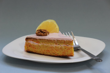 Sweet homemade carrot cake. Close up carrot cake with whipped frosting. Healthy carrot cake. Slice of carrot cake with walnuts and lemon. Homemade sponge cake on white plate. Shallow depth of field.