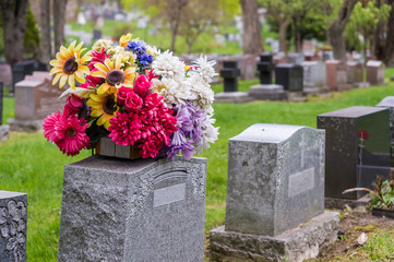 Flowers on a tombstone in a cemetary with headstones in the background - obrazy, fototapety, plakaty