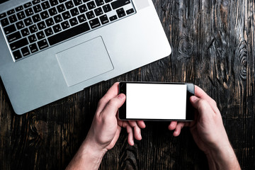 grey notebook and hands holding smartphone on dark wooden table top view