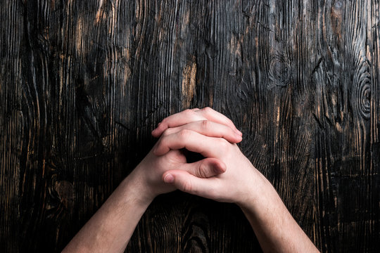 human hands folded like lock on dark wooden table