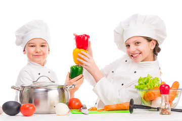two little cooks in uniform playing vegetables for soup in the kitchen