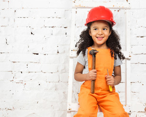 smiling little girl in helmet with hammer and screwdriver sitting on ladder