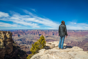 Fototapeta premium Grand Canyon, Arizona - March 21st 2014 - A young woman observing the huge canyon in front of him in south rim of the Grand Canyon National Park, Arizona, USA