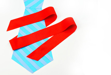 Father’s Day image of paper cutouts in two shades of blue creating a striped men’s tie. A red ribbon wraps cheerfully around the tie. Isolated on white with vertical composition. Copy space.