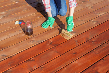 Woman applying protective varnish or wood oil on a patio wooden floor, house maintenance concept....