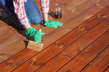 Woman applying protective varnish or wood oil on a patio wooden floor, house maintenance concept. Before and after effect