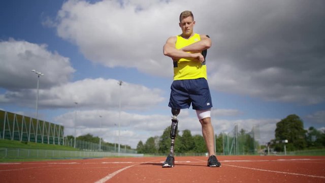  Portrait of disabled athlete with prosthetic leg standing at running track. Shot on RED Epic.