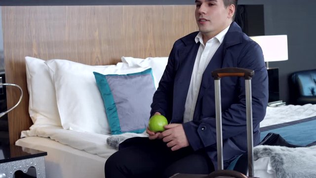 My First Business Trip/The young manager goes into the room, sits on the bed. He is carrying a green apple, and begins to eat it