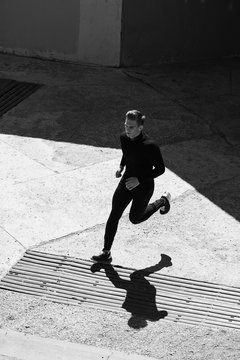 Black-and-white photo of the athlete in tight clothes running in the walls of the city