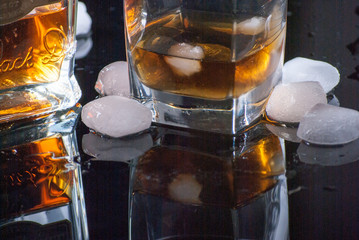 Whiskey Glass - Scotch Glass with ice cubes and Whiskey bottle with background and shinny reflection on bottom