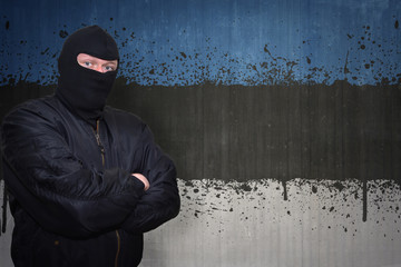 dangerous man in a mask standing near a wall with painted national flag of estonia