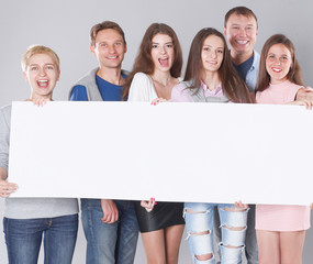 Happy young group of people standing together and holding a blank 
