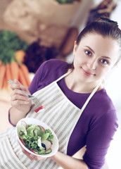 Young woman eating fresh salad in modern kitchen
