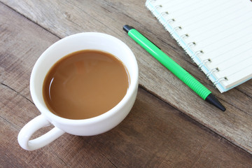 White coffee cup and have empty book,green pen on a wooden floor