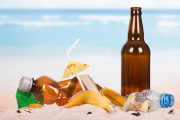 Beer bottle, food and household waste in sand on seashore.