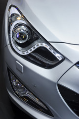 Obraz na płótnie Canvas Сar headlight, hood and bumper with plastic air intake of powerful sports car with silver metallic glossy bodywork 