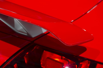 Curved spoiler of aggressive powerful sport car with red bodywork, selective focus 