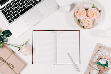 Workspace with diary, pen, vintage white tray, pink rose, gift in parchment on white background. Top view, flat lay