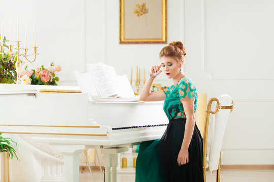 Beautiful young attractive woman in dress playing white piano
