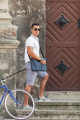 Obraz na płótnie Canvas Handsome young man is climbing the stairs approaching to a beautiful rustic door. His bicycle is leaned against a wall.