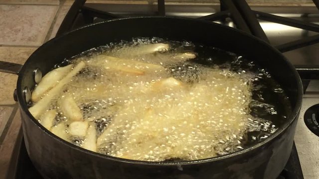 HD Video of Medium sized Russet potatoes peeled, sliced and frying in hot oil creating home made french fries. An inexpensive alternative to fast food restaurants.