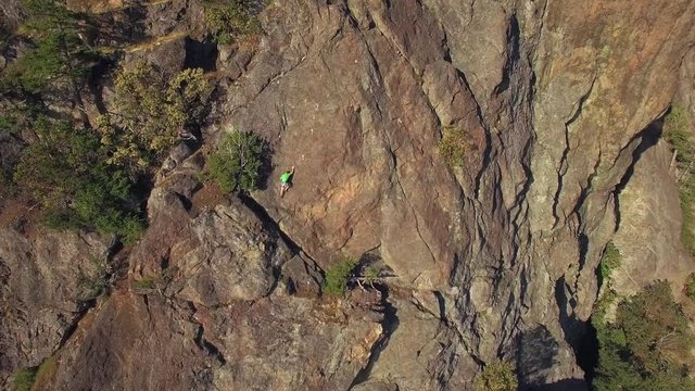 Aerial of Rock Climber Maneuvering Up Mountain Cliff on Sunny Day