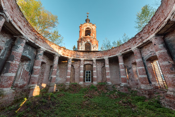 Ancient rotunda with columns without a dome on the bell tower of the background and blue sky at sunset. Abandoned brick temple overgrown with grass