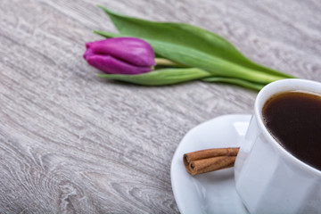 A cup of coffee with cinnamon and purple tulips
