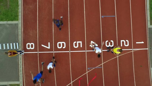  Aerial view of track athletes at running track, competing in a race & crossing finish line. 