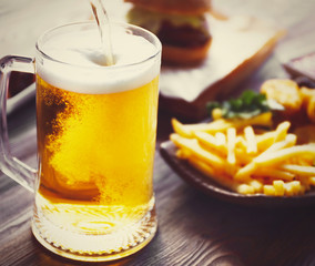 Glass mug of light beer with snacks on dark wooden table. Retro stylization