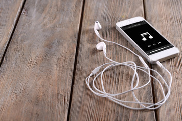 White smart phone with headphones on wooden background