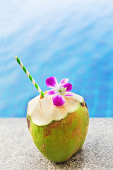 Obraz na płótnie Canvas Fresh coconut drink with orchid flower near swimming pool