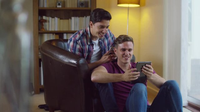 Attractive young gay couple relaxing at home, talking and using technology