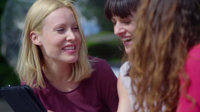  Happy attractive female friends using tablet computer outdoors