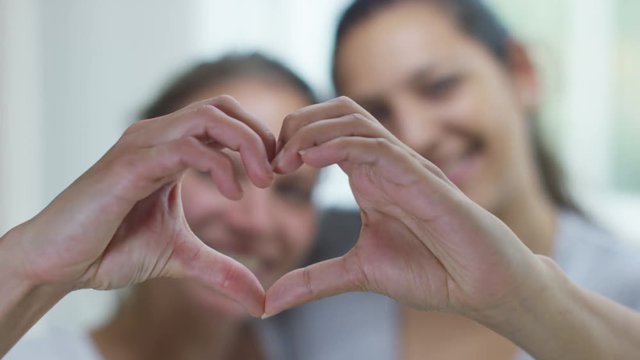  Portrait of young gay couple at home making a heart shape with their hands.