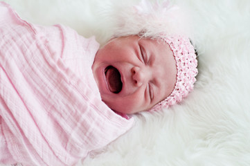 Close up of newborn baby girl in pink crying.