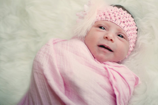 Close up of newborn baby girl in pink with funny expression.