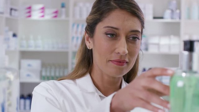  Worker in a pharmacy checking stock & putting bottles on shelves