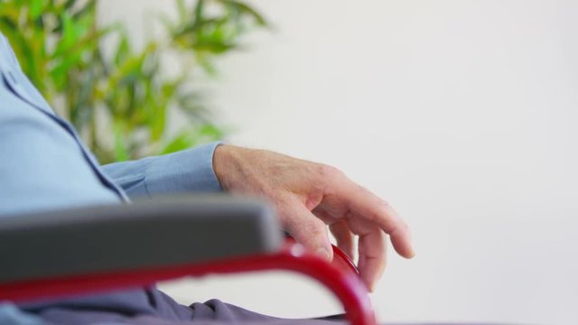  Close up on hand of elderly man sitting alone in a wheelchair. 