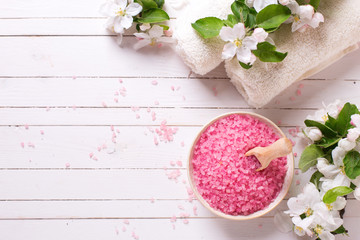 Pink sea salt in bowl, towels  and flowers on white wooden backg