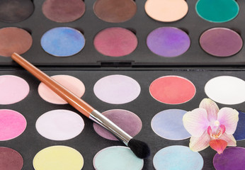 Eyeshadow palette with brush for makeup and orchid flower.