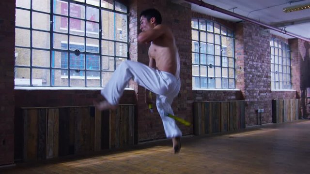  Young Asian martial artist training alone, practising his moves with nunchaku
