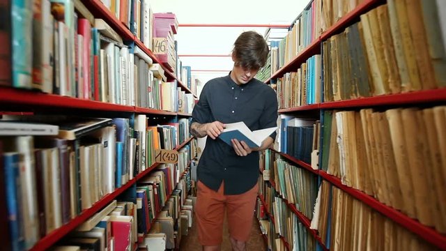 Student choosing and listing book between long bookshelves