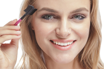 beautiful blonde woman smiling while using eyebrows comb